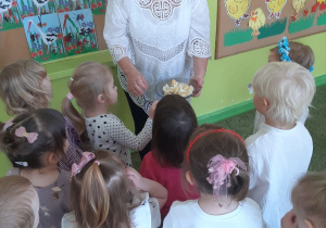 Nauczycielka zapoznaje dzieci z wielkanocną tradycją dzielenia się jajkiem i składa im życzenia świąteczne